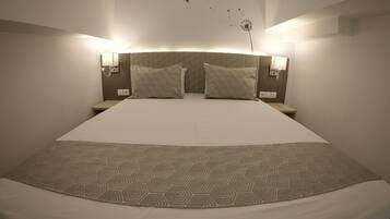A neatly made bed with patterned bedding, two wall-mounted lamps, and a wall decal of birds and a dandelion.
