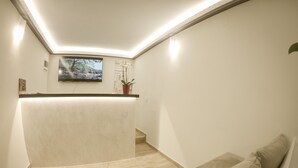 A reception area with a wooden floor, a reception desk, a wall-mounted TV, and a potted plant.