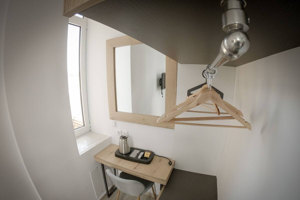 Habitación pequeña con escritorio de madera, una silla, perchero de madera colgante, espejo e iluminación en el techo.