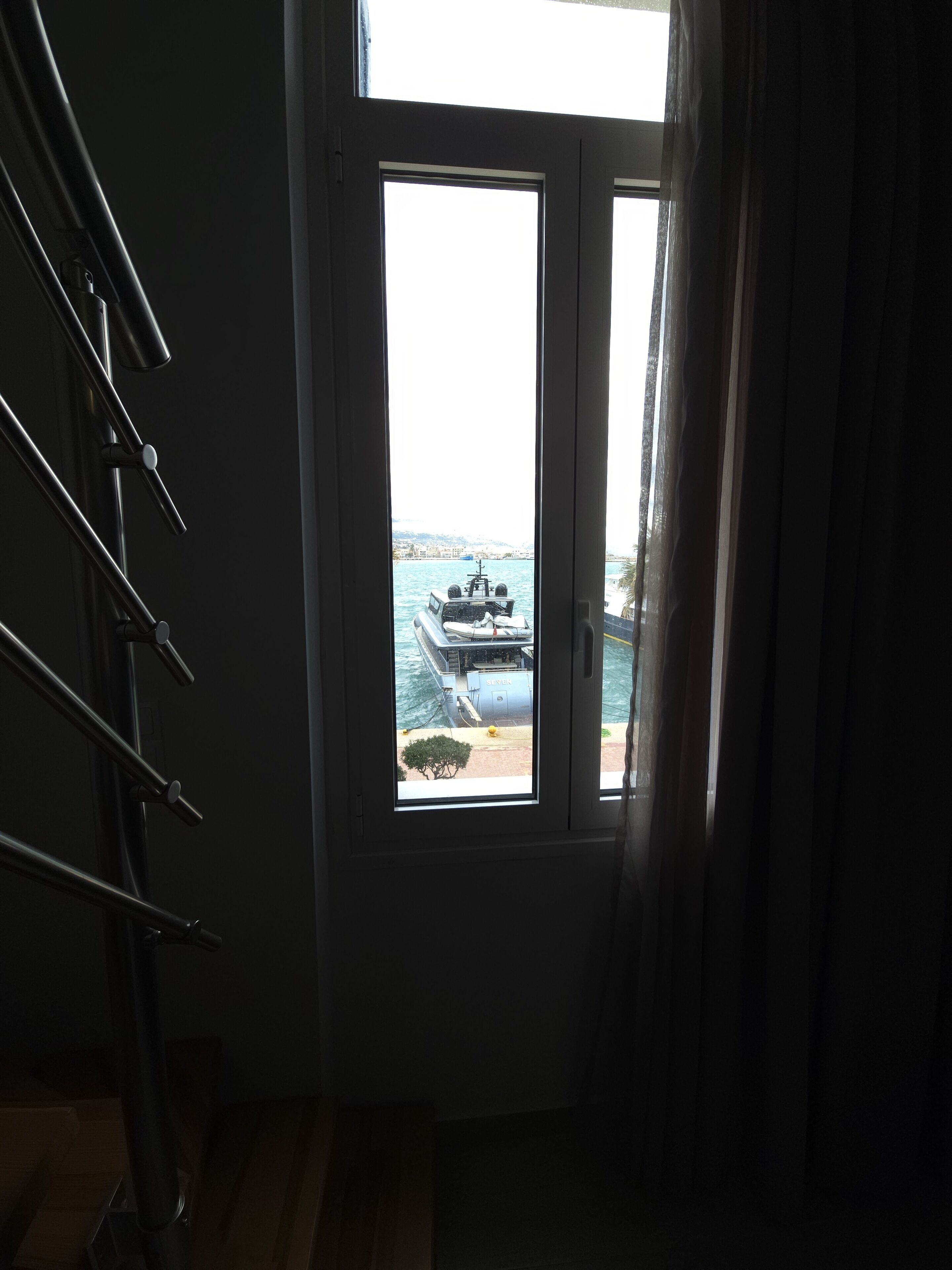 Vista a través de una puerta con ventana, que muestra un barco y una costa lejana.