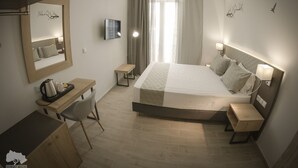 A hotel room with a bed, bedside tables, a desk, a chair, a TV, and a window with curtains.