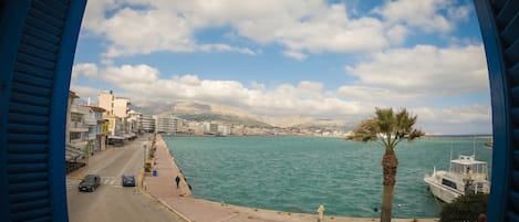 A coastal cityscape with a clear view of the sea, buildings, and a palm tree.