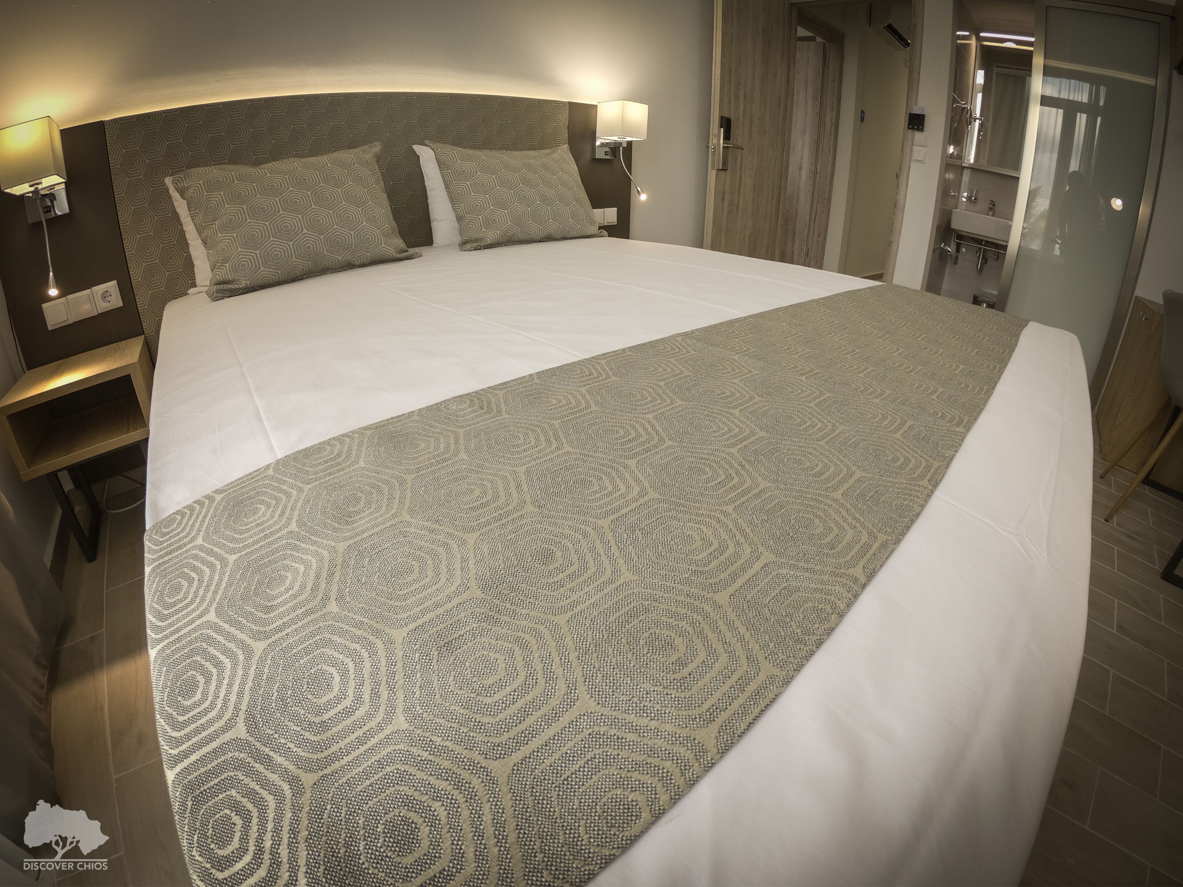 Een groot bed met een gebedruid sprei, twee bedlampen en een houten hoofdbord.