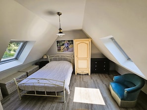 A bedroom with a sloped ceiling, a bed, a chair, a dresser, and a window. - "La Mouette" Vacation Rental - Veranda - Green Surroundings - Beach (Trévou-Tréguignec)