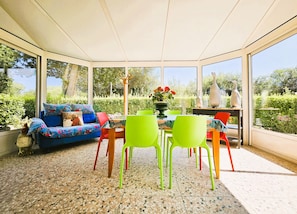 A conservatory with a blue sofa, green chairs, and a dining table. - "La Mouette" Vacation Rental - Veranda - Green Surroundings - Beach (Trévou-Tréguignec)