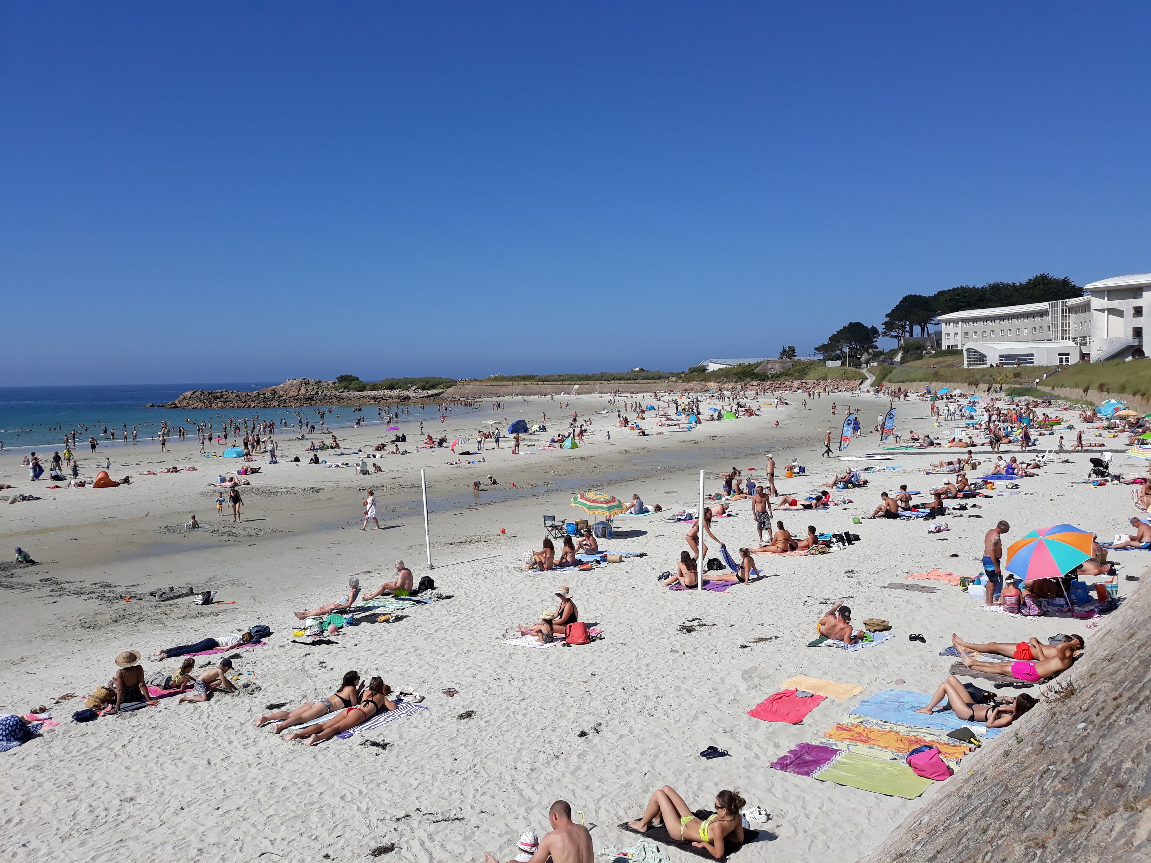 Una spiaggia affollata, con persone che prendono il sole e si fanno il bagno.