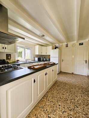 A kitchen with a central island, white cabinetry, a gas stove, and a granite countertop. - "La Mouette" Vacation Rental - Veranda - Green Surroundings - Beach (Trévou-Tréguignec)