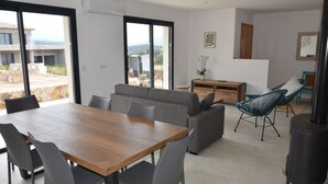 Ein modernes Wohnzimmer mit einem Holzesstisch, grauen Sofas und einem schwarzen Kaminofen.