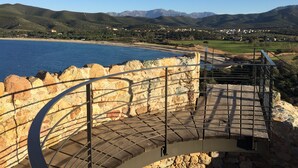 Eine Küstenansicht mit einer Steintreppe, die zu einem Balkon mit Blick auf das Meer und die Berge führt.