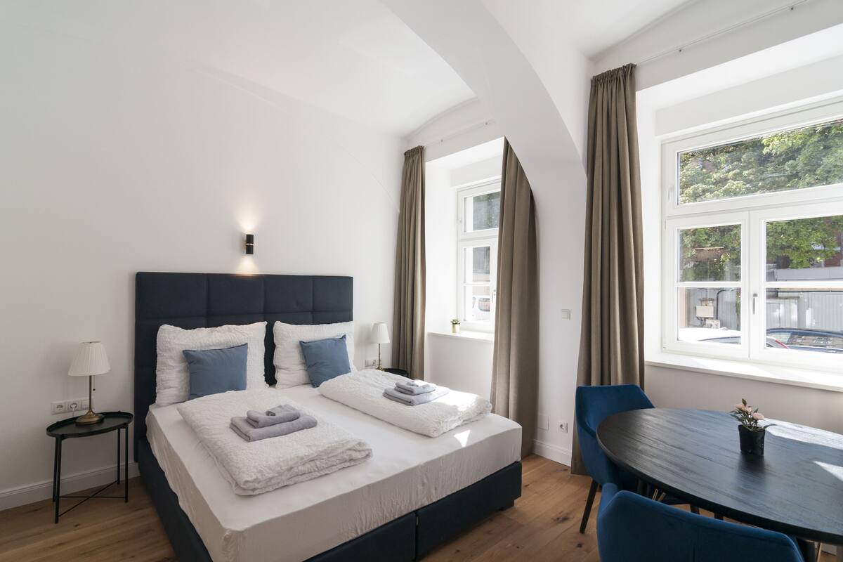Quarto de hotel moderno com uma cama grande, uma mesa pequena e vista para o exterior.