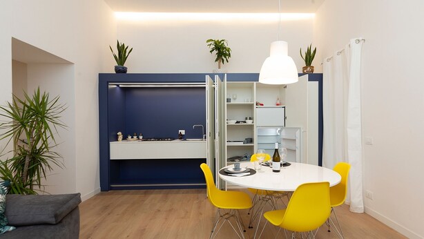 A compact dining area with a round table, yellow chairs, and a white pendant light. - MASSIM'HOME HOUSE NEAR THE THEATRE (Palermo)