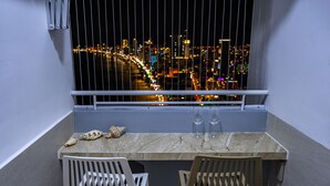 A balcony with a view of a cityscape at night. There is a table with two chairs and two wine glasses on it. - The Sea House Nha Trang (Nha Trang)