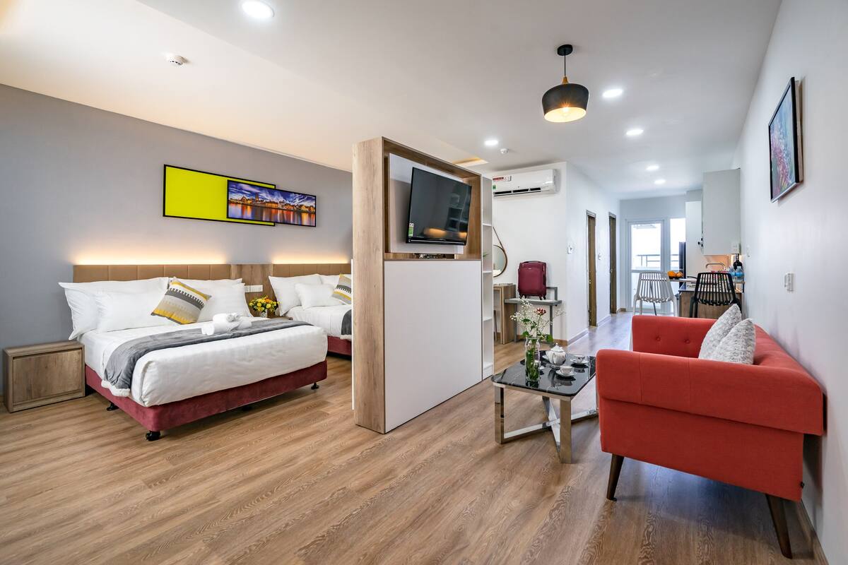 Een moderne hotelkamer met een groot bed, een rode fauteuil, een televisie en een eethoek op de achtergrond.