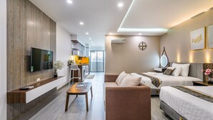 A modern hotel room with a flat-screen TV, a sofa, a bed, and a dining area with a kitchen in the background. - The Sea House Nha Trang (Nha Trang)