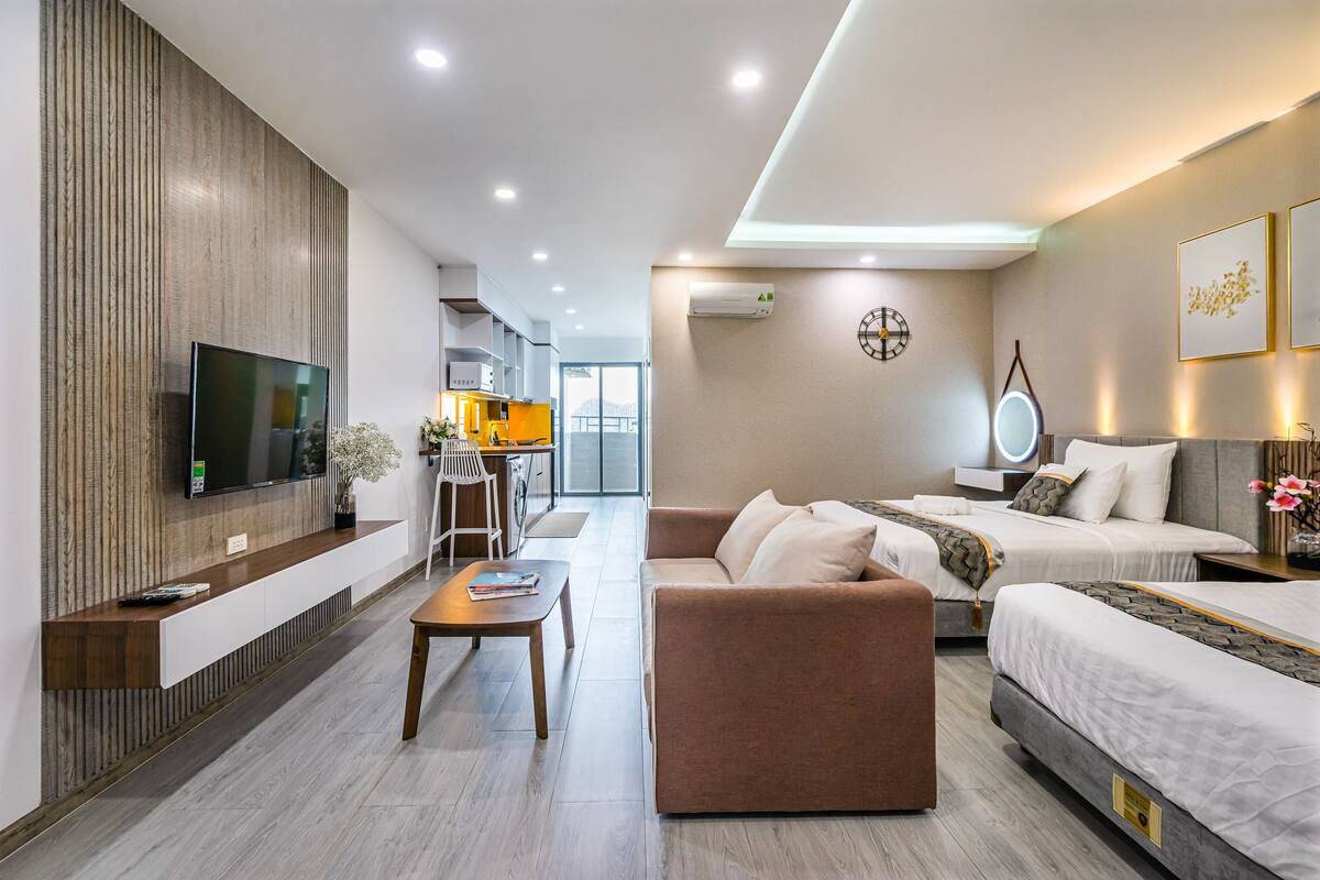 Een moderne hotelkamer met een flatscreen televisie, een bank, een bed en een eethoek met een keuken op de achtergrond.