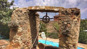 A rustic stone structure with a swing, a pool, and a white chair in the background. - La Rajoleria d'Esclanyà, rural house with private swimming pool on the Costa Brava (esclanyà)