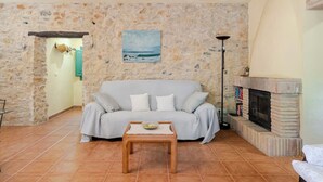 A living room with a stone wall, a sofa, a coffee table, a fireplace, and a painting of a beach scene. - La Rajoleria d'Esclanyà, rural house with private swimming pool on the Costa Brava (esclanyà)
