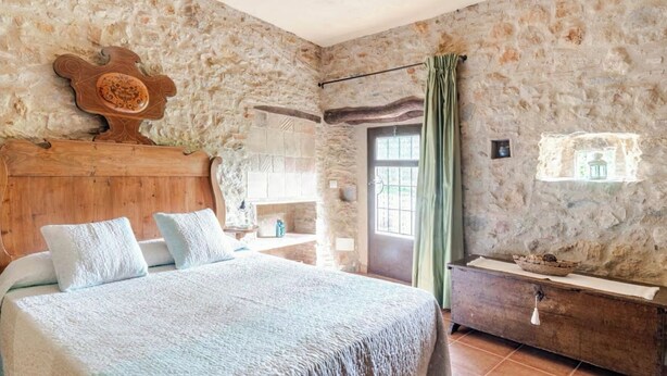 A bedroom with a stone wall, a wooden bed, a nightstand, and a green curtain. - La Rajoleria d'Esclanyà, rural house with private swimming pool on the Costa Brava (esclanyà)