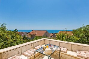 A balcony with a glass table, cushions, and a view of the sea and houses. - Rooms on Konalu (Dubrovnik)