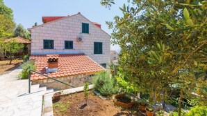 A two-story house with a red-tiled roof, white walls, and green shutters. There is a small garden with potted plants and a stone staircase leading to the entrance. - Rooms on Konalu (Dubrovnik)