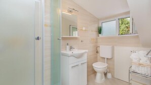 A modern bathroom with a glass shower enclosure, a white sink, a toilet, and a window above the toilet. - Rooms on Konalu (Dubrovnik)