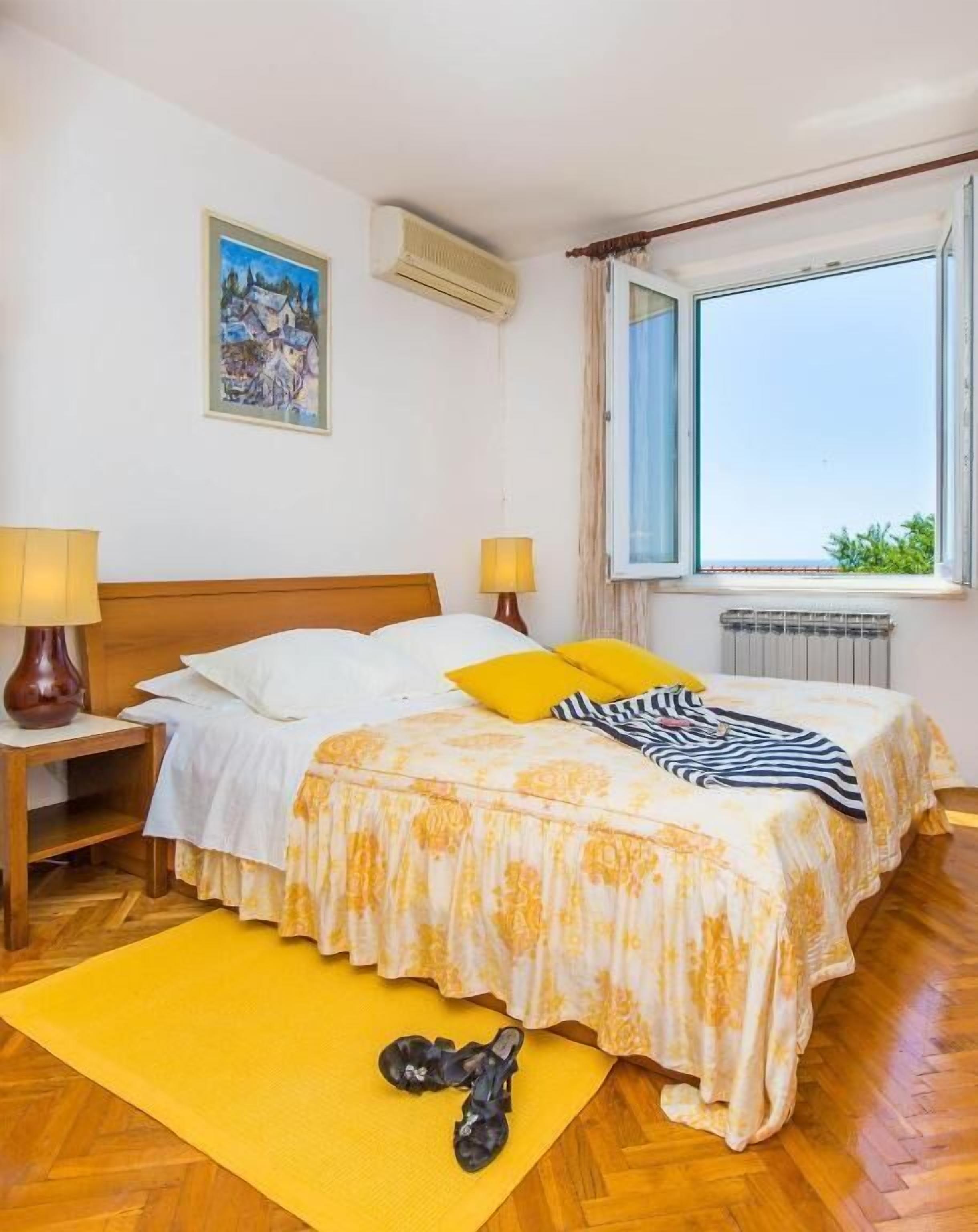 A bedroom with a bed, bedside lamps, a window, a radiator, and a painting on the wall.