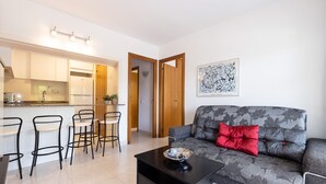 A modern living room with a grey sofa, a coffee table, and a dining area with bar stools. - Beachfront Apartment for 4 people with Air Conditioner - UHC TXINGUDI 139 (Cambrils)