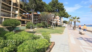 A coastal residential area with multi-story buildings, a paved walkway, and palm trees. - Beachfront Apartment for 4 people with Air Conditioner - UHC TXINGUDI 139 (Cambrils)