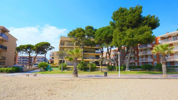 A beachfront hotel with multiple floors, outdoor seating, and palm trees. - Beachfront Apartment for 4 people with Air Conditioner - UHC TXINGUDI 139 (Cambrils)