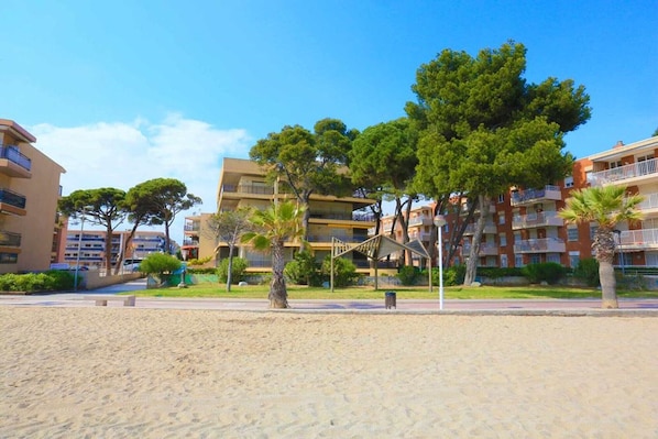 Un hotel frente a la playa con varios pisos, terraza al aire libre y palmeras.