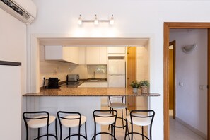 A modern kitchen with a granite countertop, four bar stools, a built-in oven, and a refrigerator.