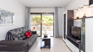 A modern living room with a sofa, a coffee table, a flat-screen TV, and a dining area visible through the glass door. - Beachfront Apartment for 4 people with Air Conditioner - UHC TXINGUDI 139 (Cambrils)