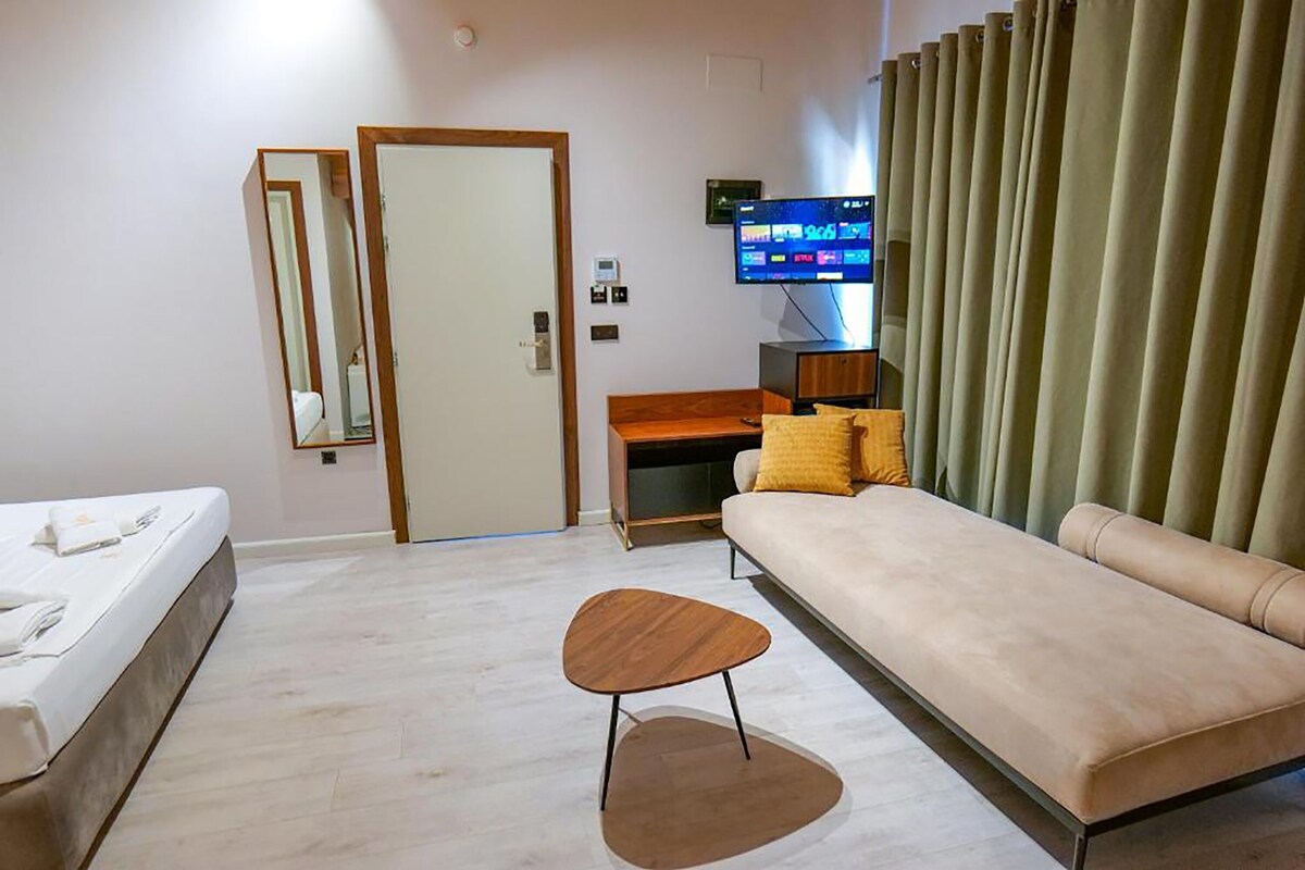 Una habitación de hotel con una cama, un sofá, una pequeña mesa de madera, un televisor y una puerta.