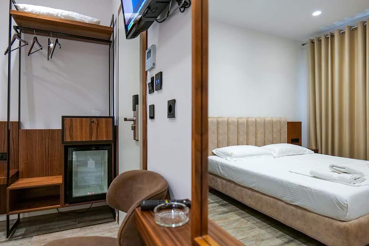 A hotel room with a bed, a desk with a chair, a television mounted on the wall, and a small refrigerator.