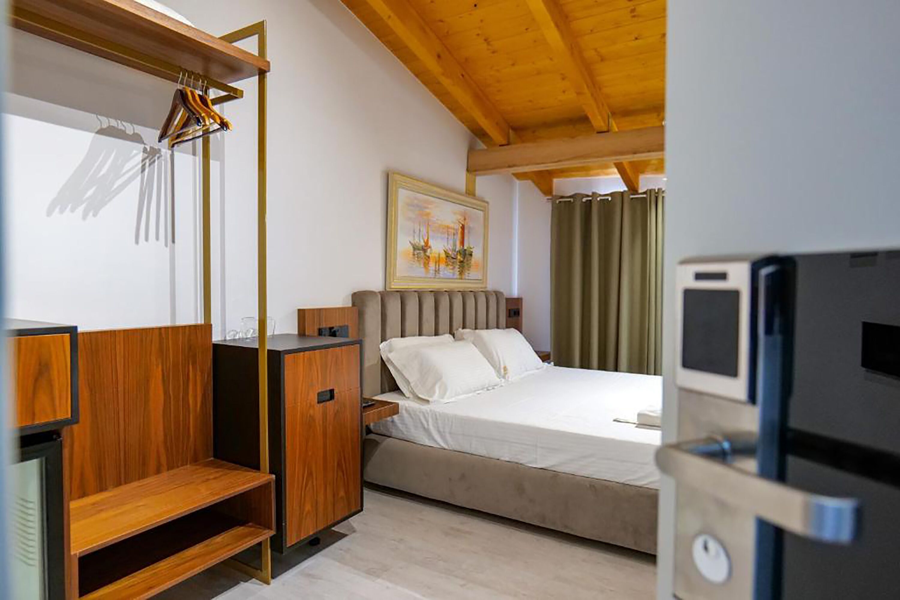 A bedroom with a bed, a wooden wardrobe, a desk, a chair, a painting, and a television.