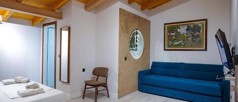 A hotel room with a bed, a blue sofa, a wooden chair, a painting, and a sign on the wall.