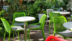 Un patio con sillas de metal verde y mesas blancas, rodeado de abundante vegetación.