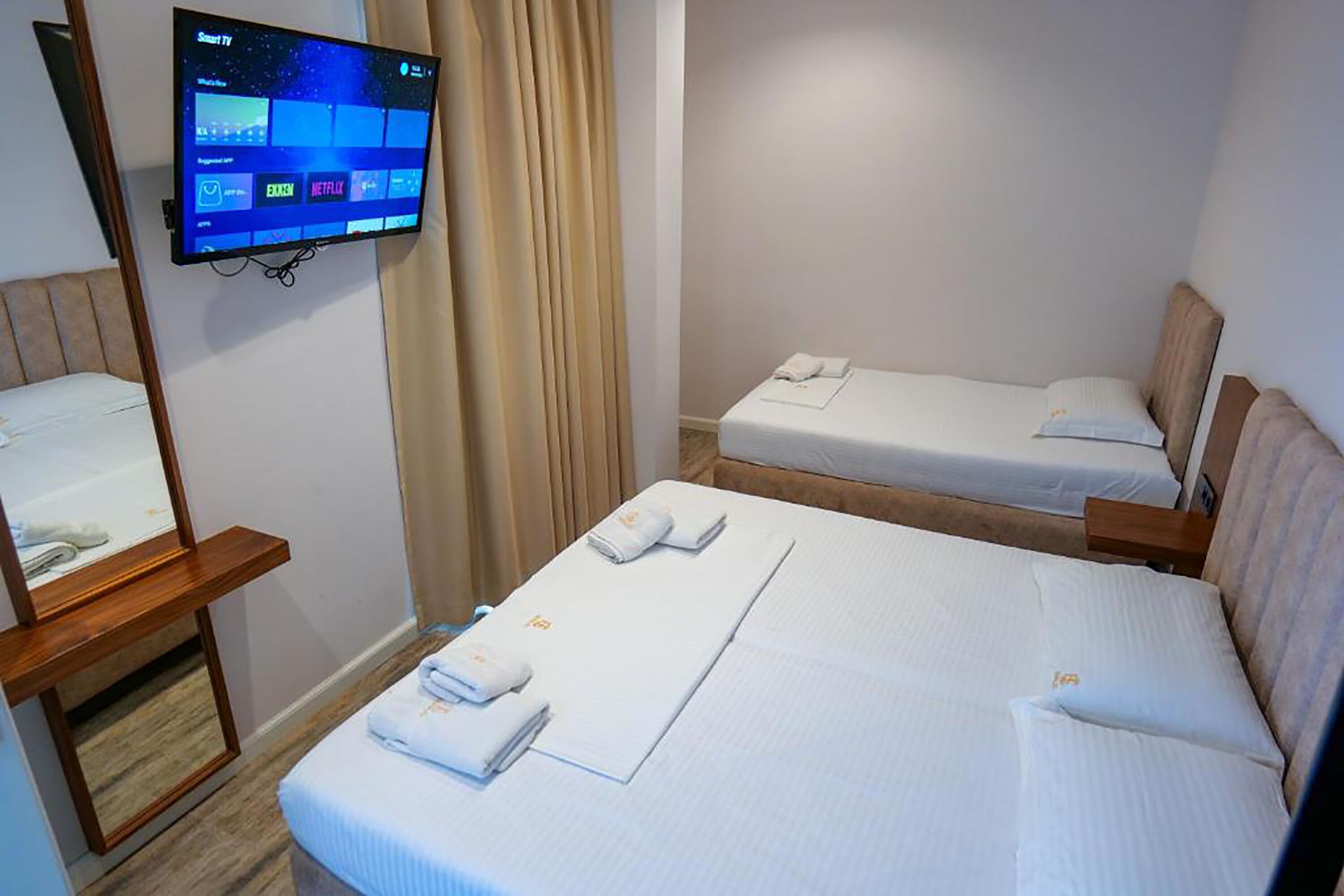 A hotel room with two beds, a TV mounted on the wall, and a wooden nightstand.