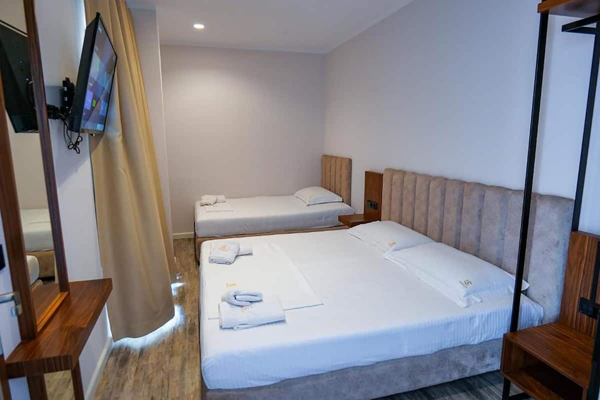 A hotel room with two single beds, a TV mounted on the wall, and a wooden headboard.