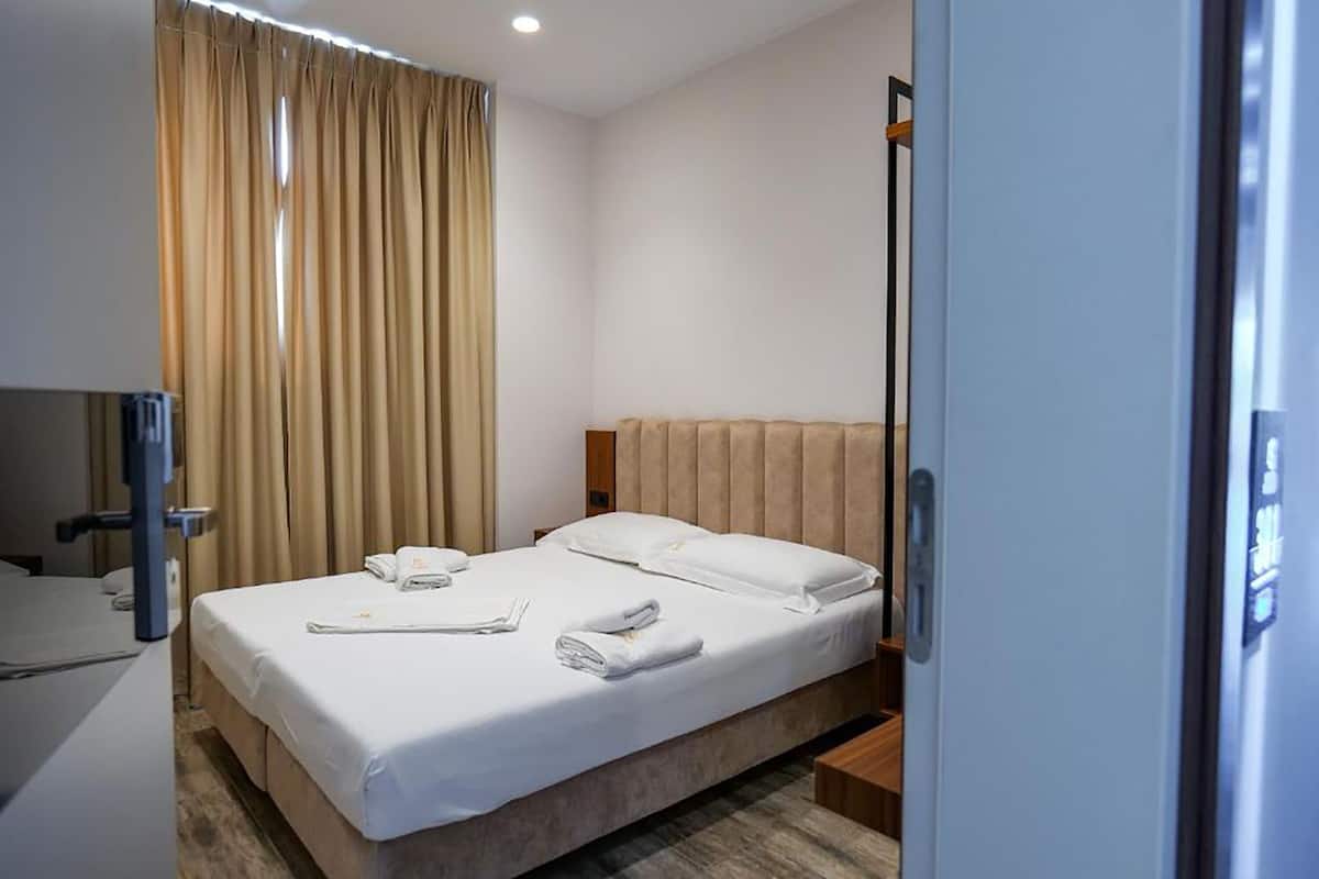 A hotel room with a bed, a bedside table, a lamp, and a window with curtains.