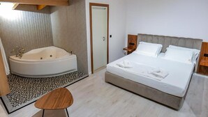 Un dormitorio con una cama grande, un baño independiente con bañera y un pequeño taburete de madera.