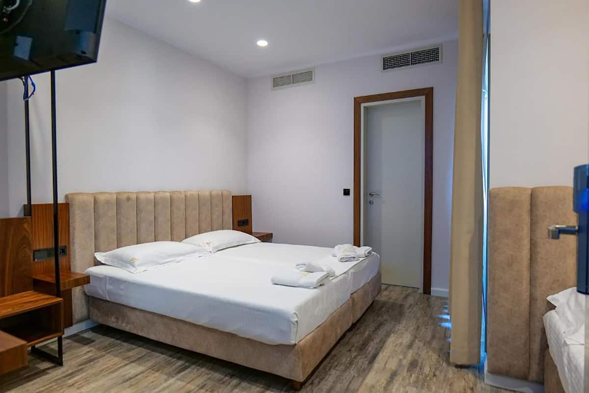 A hotel room with a bed, a TV, a wooden nightstand, and a door.