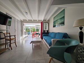 A modern living room with a sofa, a television, and a dining area with chairs and a table. - "Le Macareux" Vacation Rental & Chalet: Lush, Green Setting—Beach Within Walking Distance (Trévou-Tréguignec)