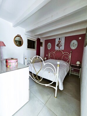 A bedroom with a white metal bed frame, a bedside table, a dresser, a mirror, and a window. - "Le Macareux" Vacation Rental & Chalet: Lush, Green Setting—Beach Within Walking Distance (Trévou-Tréguignec)
