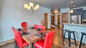 Uma sala de jantar com mesa de madeira, cadeiras vermelhas e um candelabro.