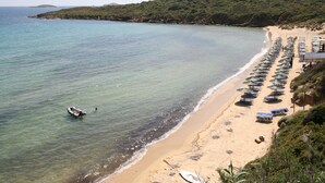 A beach with clear water, a boat, and rows of umbrellas. - Villa Maniati Studios (Andros)