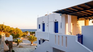 A white building with blue doors and windows, a stone-paved courtyard, and a view of the sea. - Villa Maniati Studios (Andros)
