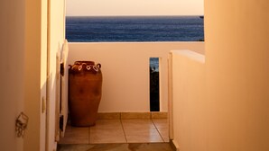 A corridor with a view of the sea through an archway, a potted plant, and a small door. - Villa Maniati Studios (Andros)