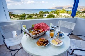Un balcon avec une table préparée pour le petit-déjeuner, comprenant des croissants, un panier de fruits et un verre de jus d’orange.