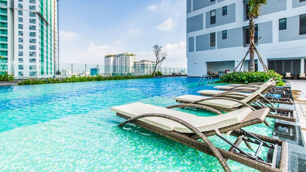 Ein Swimmingpool mit Liegestühlen und einer Palme, umgeben von modernen Gebäuden.